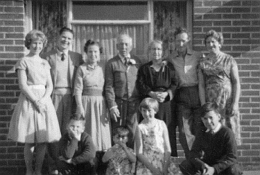 The
                family, with the visiting cousins in 1963, standing in
                front of a brick house.